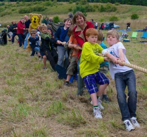 A group of around 15 children and adults pulling hard on a tug of war rope in a grassy field.