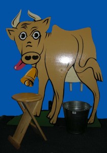 a wooden cow-shaped board with 'udders', shown with a wooden stool and metal bucket