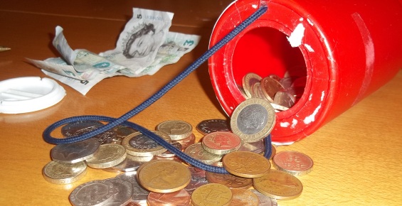 Collection tin with coins spilling out of it and notes in the background.