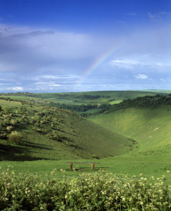 A long, curved valley between two hills, with a rainbow faintly appearing in background.